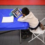 An overhead shot of a student sitting at a table staring at a laptop screen.
