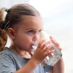 Apakah fluoride menurunkan IQ anak -anak? Penelitian baru menimbulkan pertanyaan Gadis muda minum segelas air