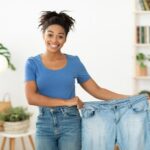 Wanita kulit hitam ramping yang bahagia menunjukkan jeans kebesaran lama setelah diet penurunan berat badan yang sukses